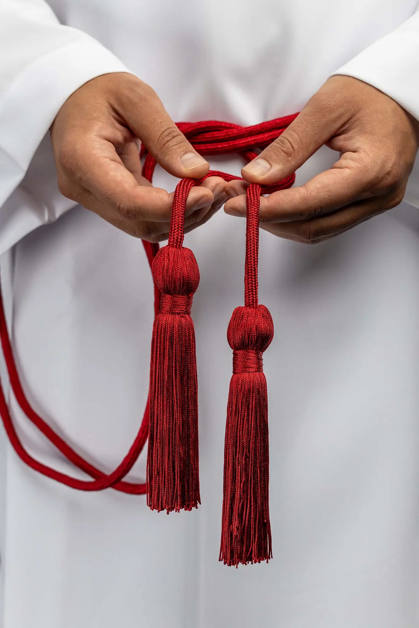 Red liturgical cincture with decorative tassels made from braided cord, tied around an alb.