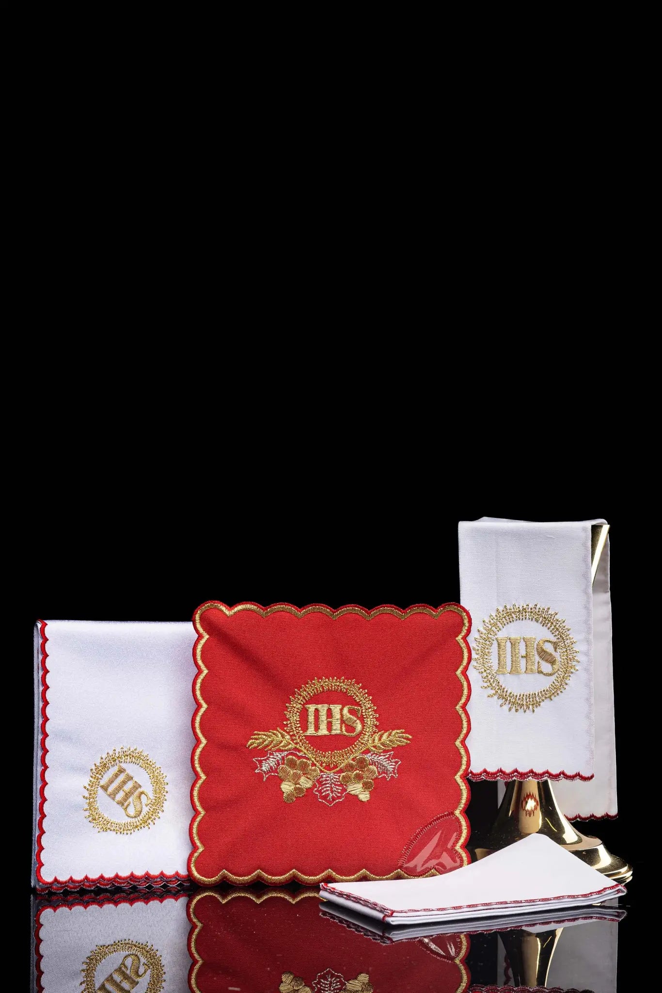 Red chalice linen set with gold IHS embroidery, including a red pall, white corporal, white purificator, and white lavabo towel, all with matching gold IHS symbols and scalloped embroidered edges.