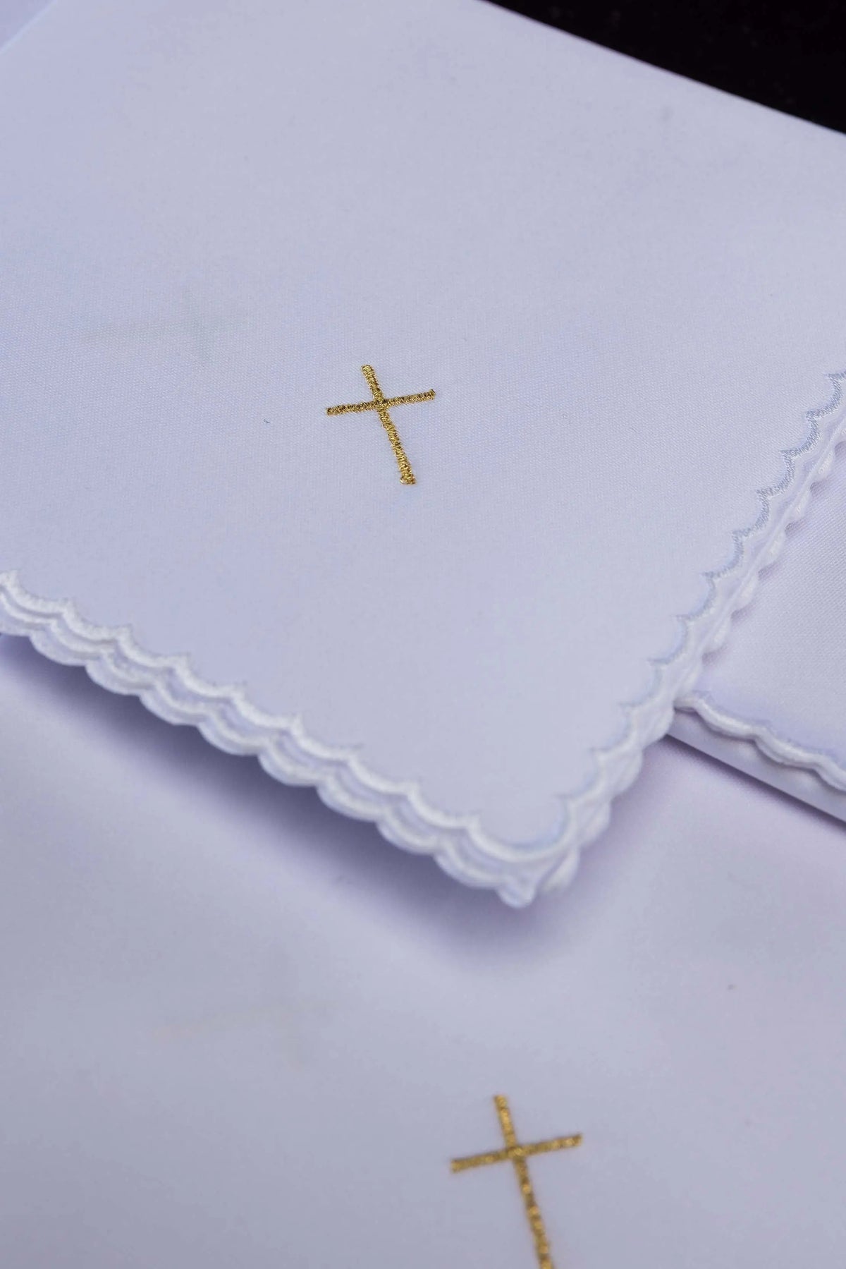 Blanc corporal avec croix brodée dorée, gros plan sur la broderie et le bord festonné