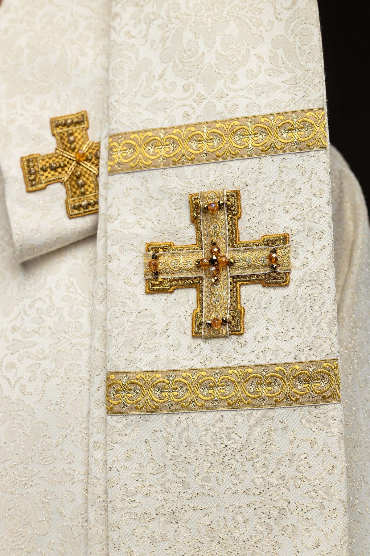 Ecru chasuble with dimensional crosses and natural stones, gold tassels close-up